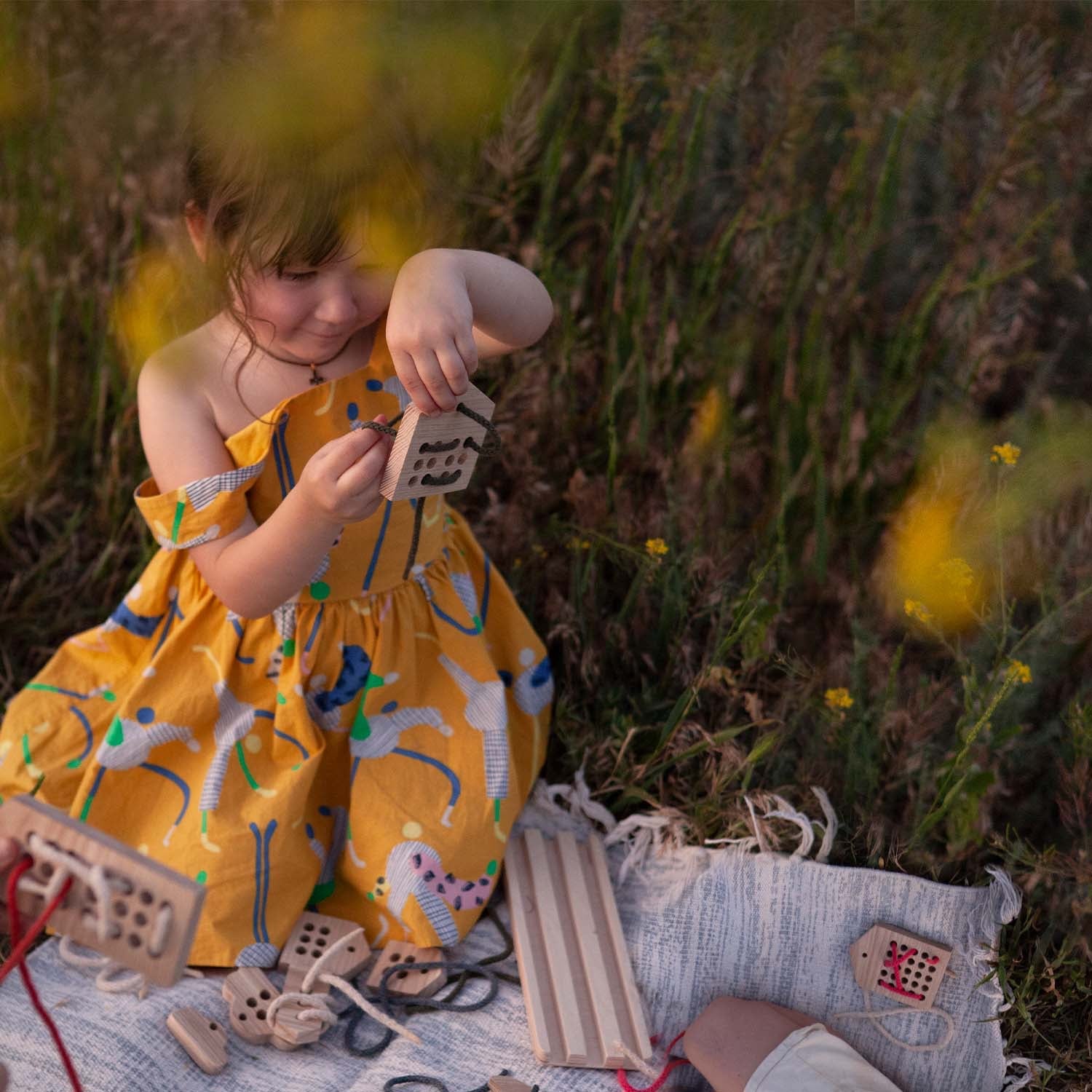 girl threading lace through a wooden house toy