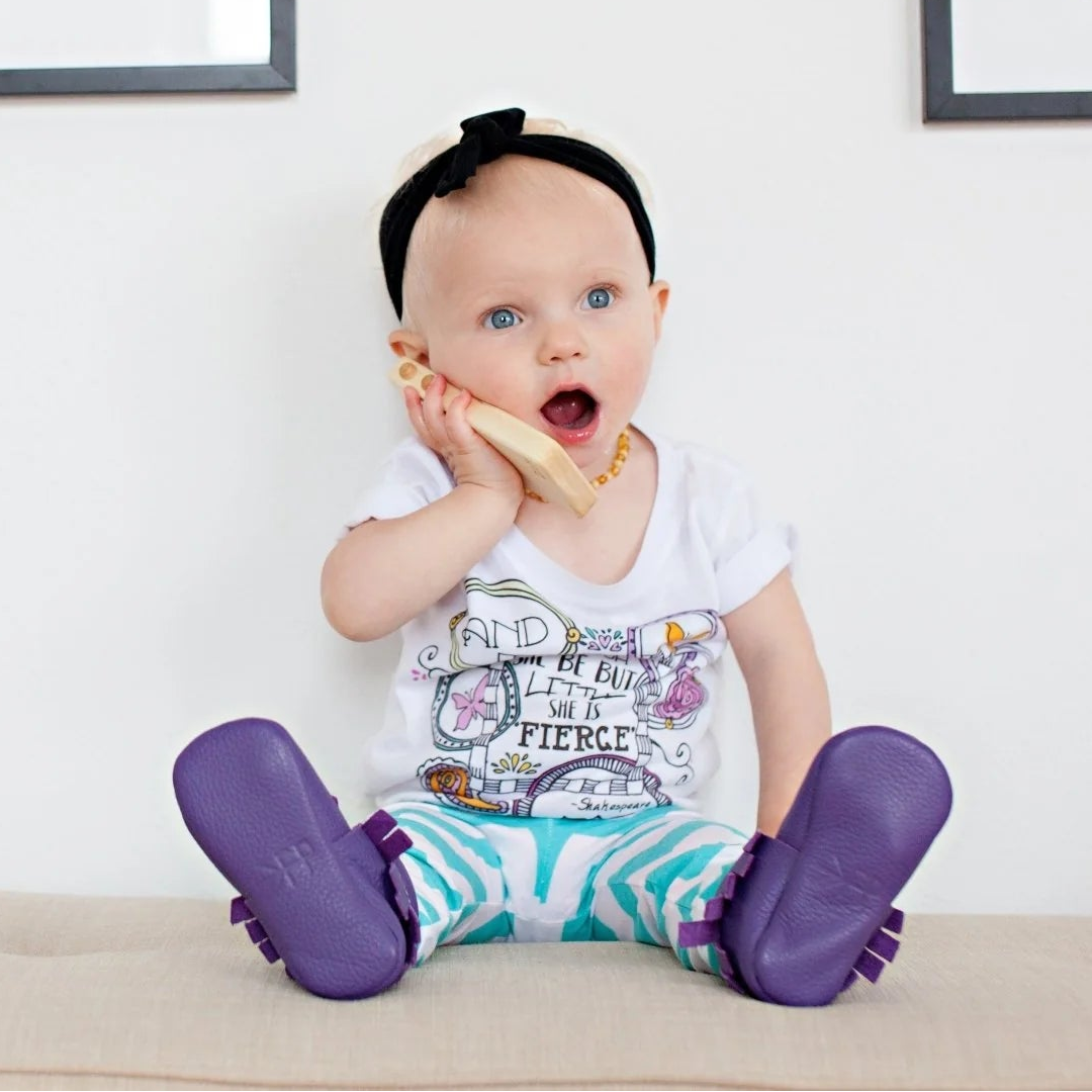 Toddler sitting on a couch pretending to talk on a wooden toy phone