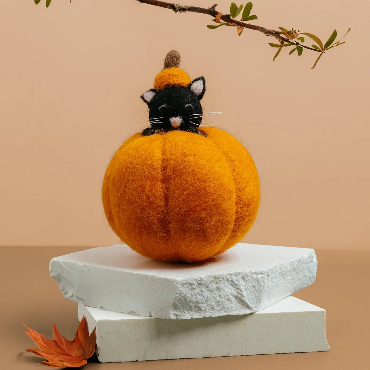 A black felt cat wearing a small orange pumpkin hat peeks out from inside a pumpkin.