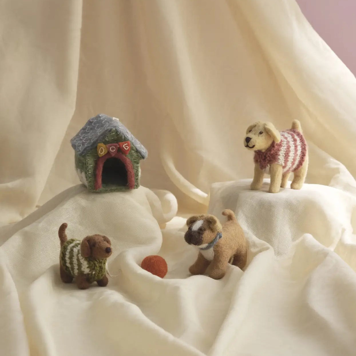 Three miniature felt toy dogs in different poses with a small doghouse nearby.