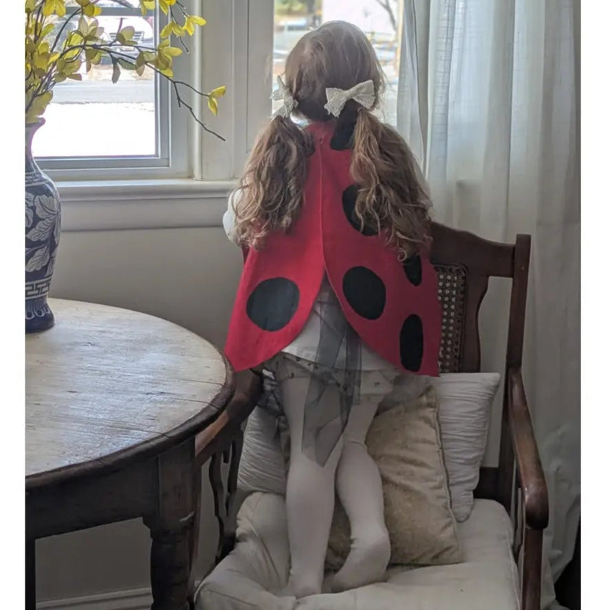 girl in a ladybug costume standing on a chair by a window