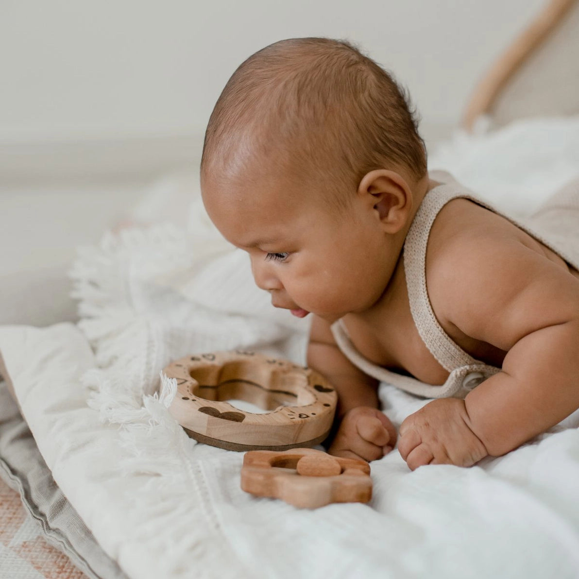 Baby looking into a wooden mirror next to a natural wood flower rattle