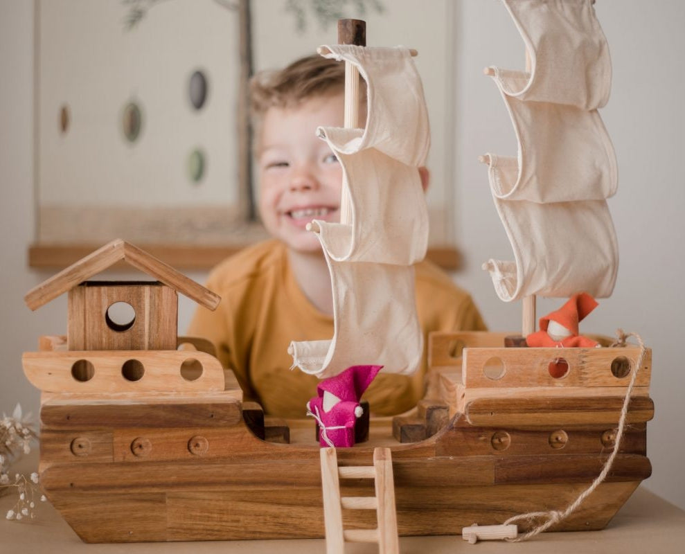 Boy playing with a wooden toy pirate ship and gnome dolls