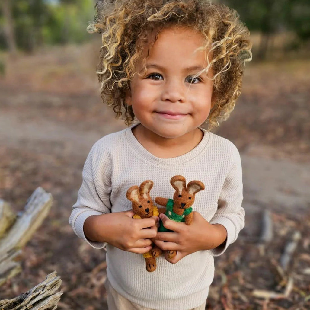 Child holding two Tara Treasures felt rabbit toys in the forest