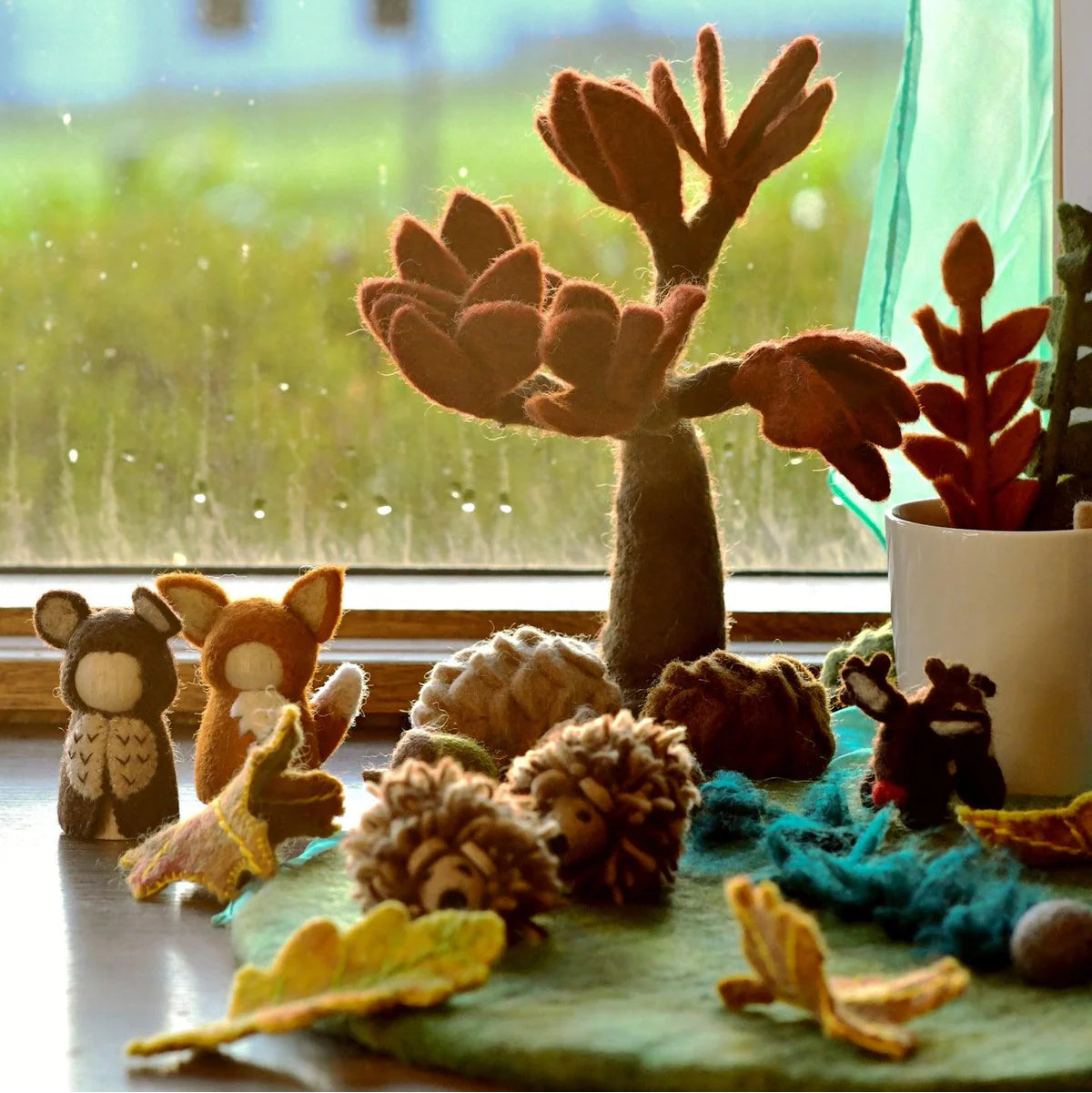 Felted animal toys and plants on a windowsill with a blurred outdoor background