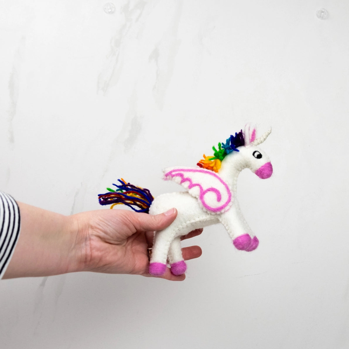 Hand holding a small unicorn plush toy with rainbow mane