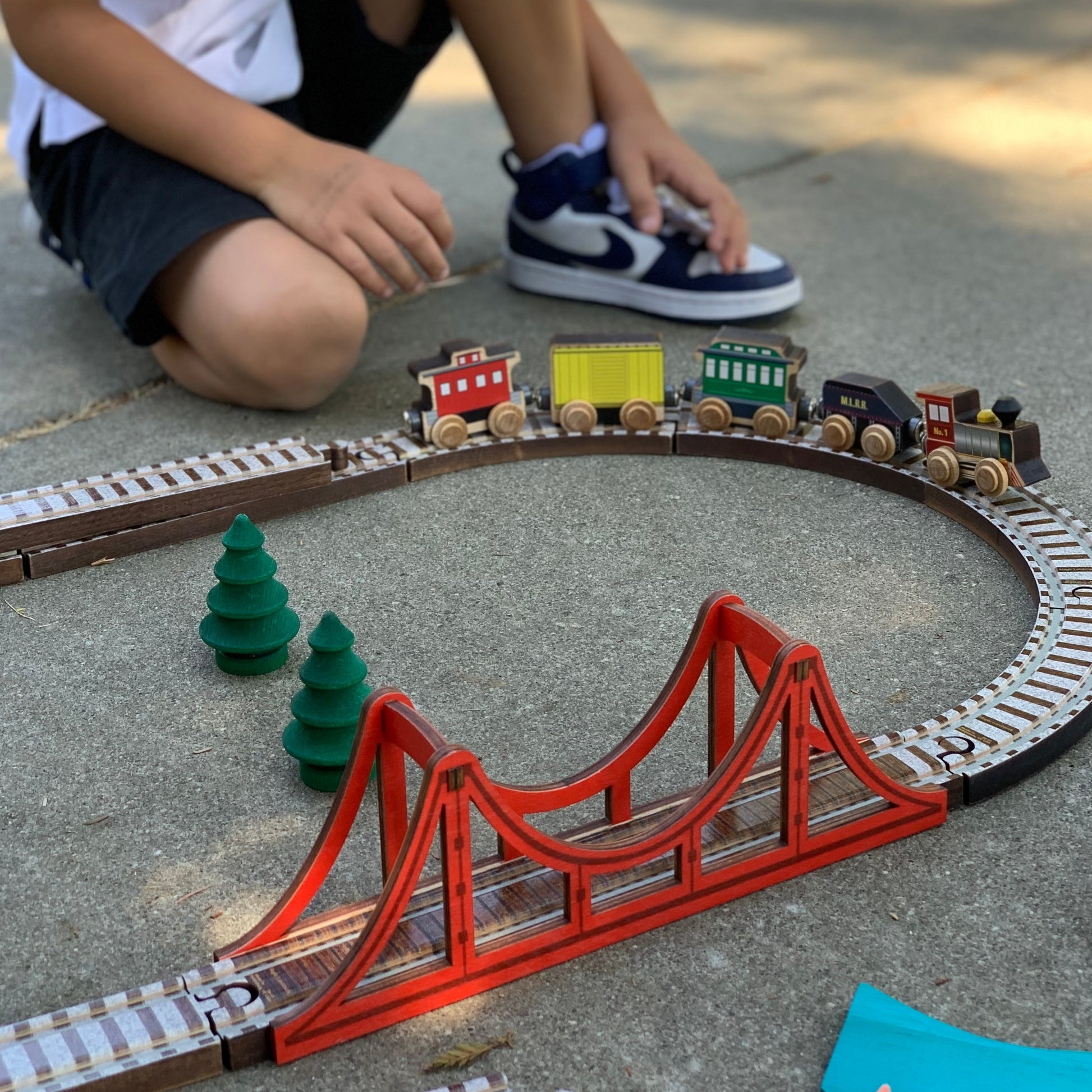 boy playing with wooden train and track with suspension bridge