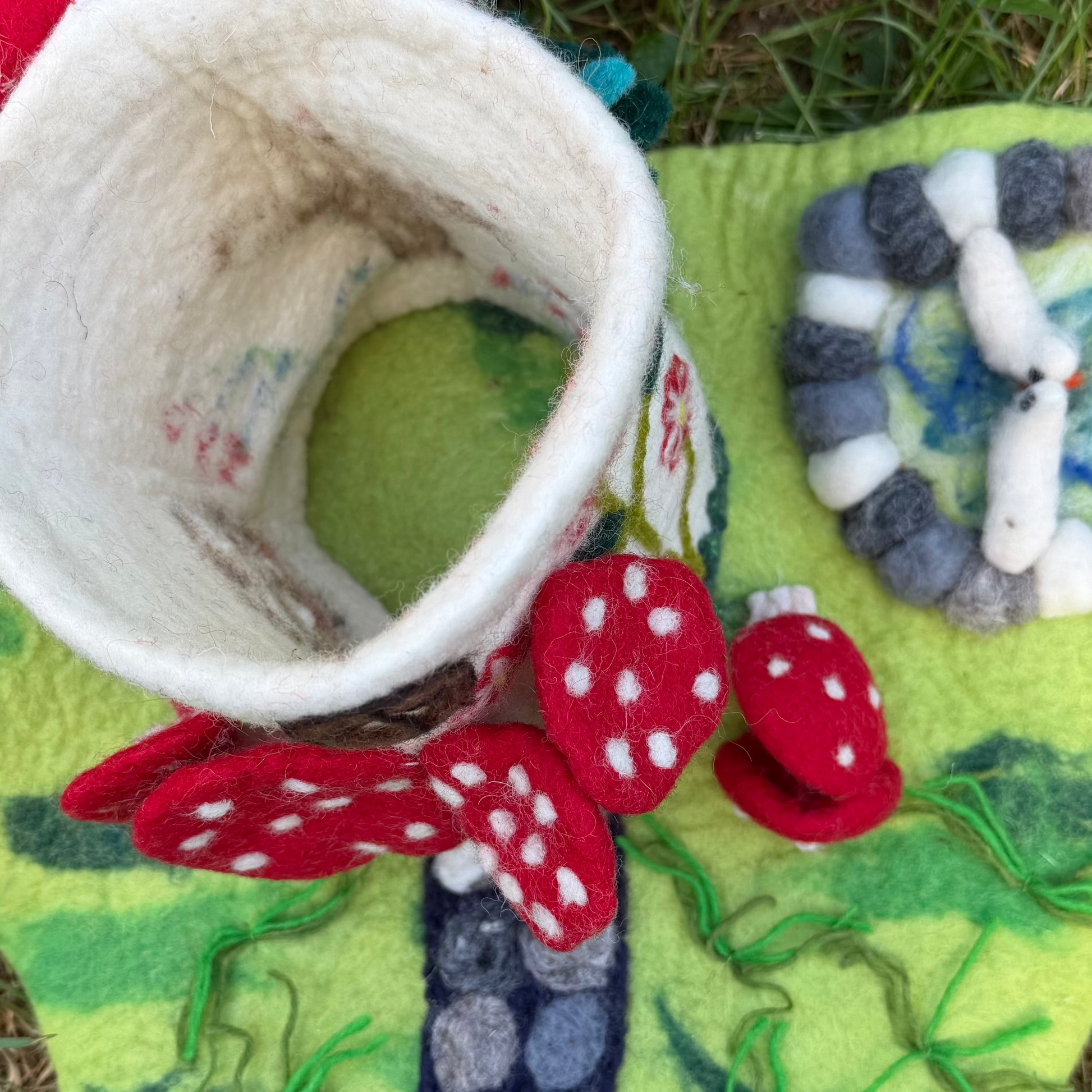felted mushroom dollhouse with the roof open on a garden playmat and birds in a pond
