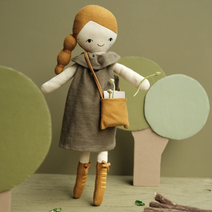 Fabelab soft stuffed acorn doll with a green dress and boots standing in a toy forest setting