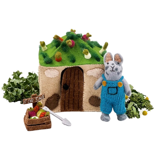 felted farmer mouse doll next to a toy house with a shovel and veggies for sale.
