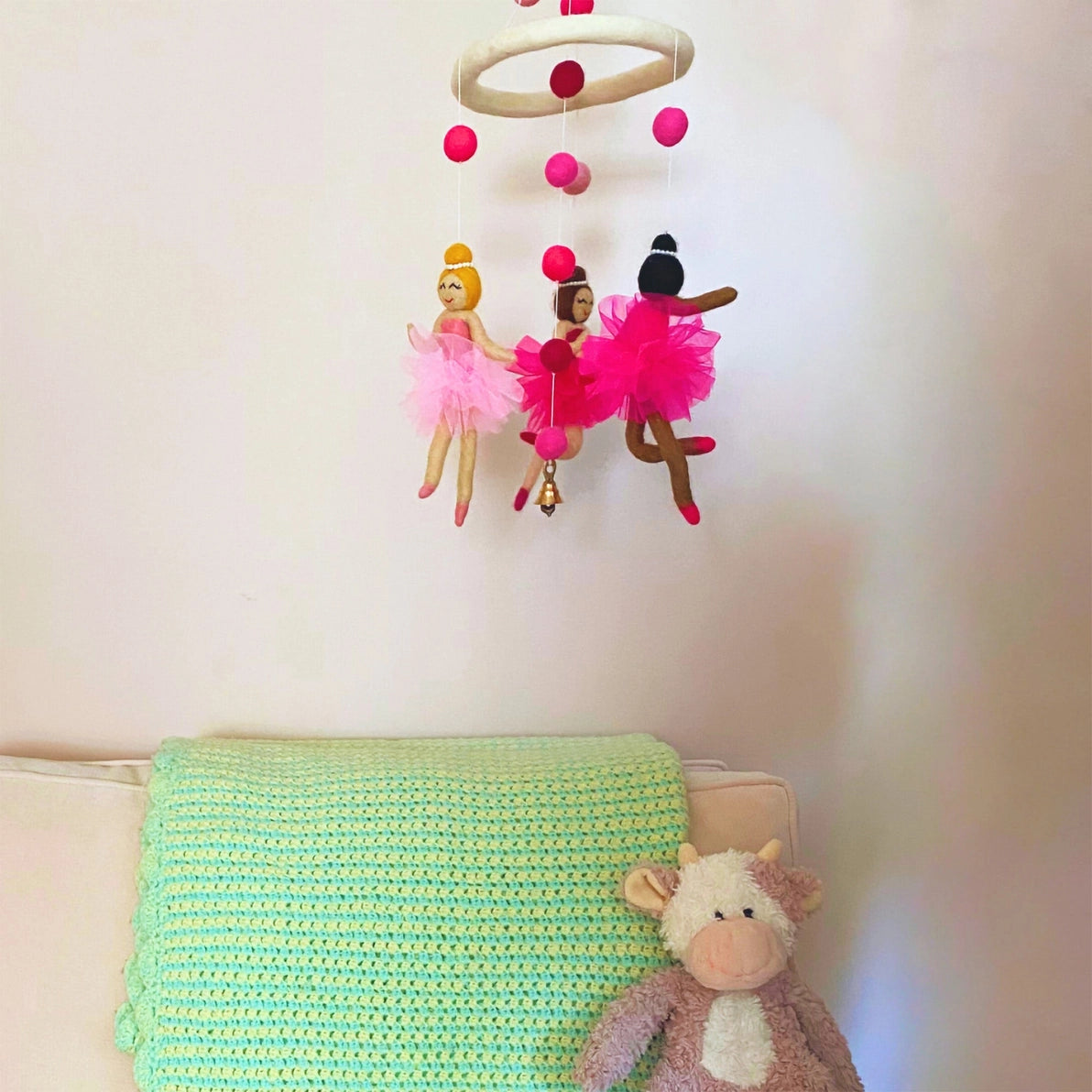 Handmade felt baby nursery mobile with diverse, multicultural ballerinas above a crib.