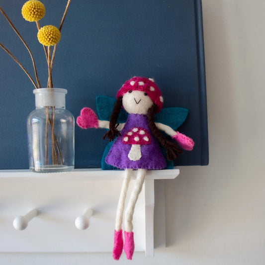 Colorful felt tooth fairy doll on a shelf with brown hair and a mushroom bonnet.