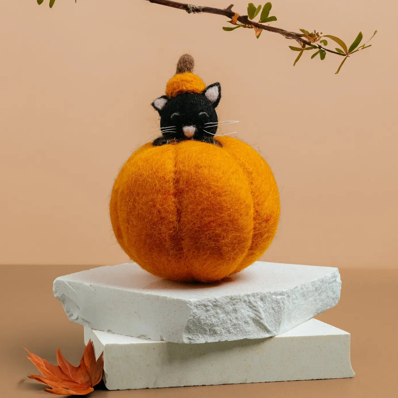 A black felt cat wearing a small orange pumpkin hat peeks out from inside a pumpkin.