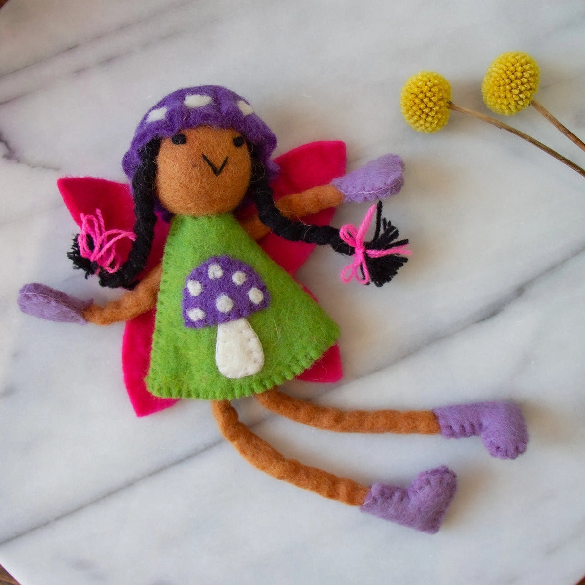 Felt tooth fairy doll with brown skin and black hair in a green dress and purple mushroom hat