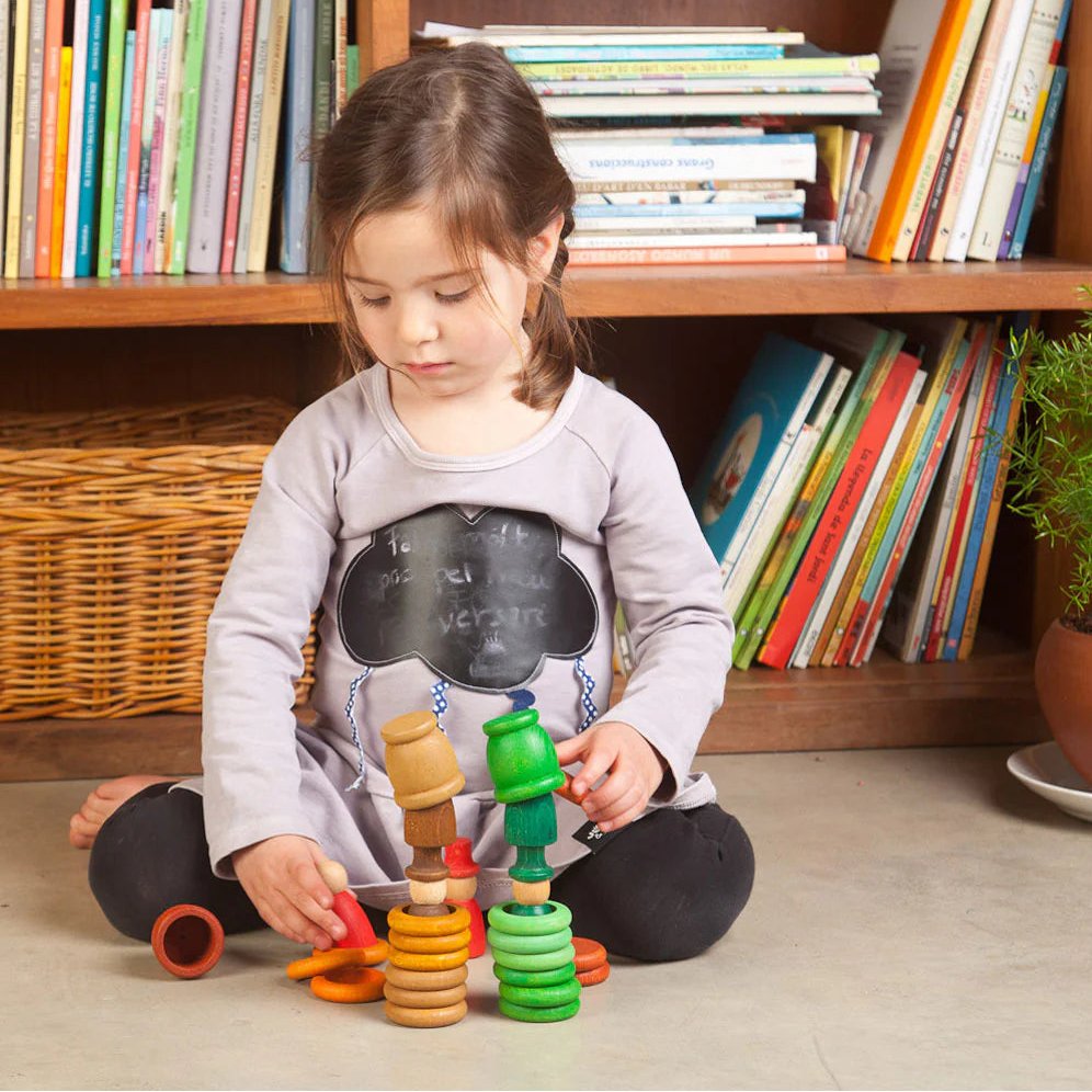 Girl playing with Grapat Autumn wooden peg doll nins, cups and rings in oranges and greens