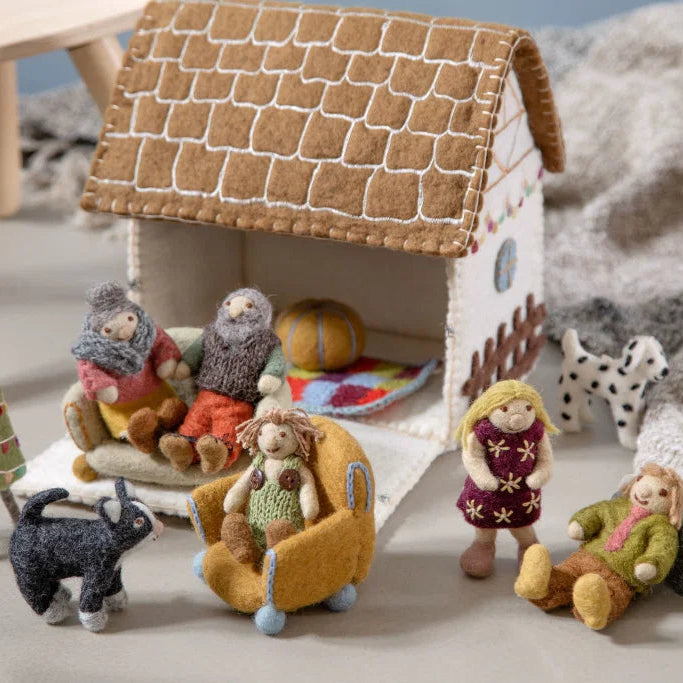 A cozy handmade felt dollhouse scene with small felt animals, a Christmas cottage  house, and several felt dolls and furniture arranged inside and around the house .
