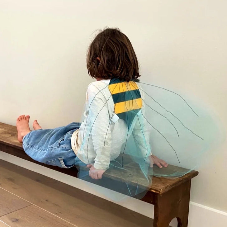 Child sitting on a wooden bench wearing bumble bee costume wings