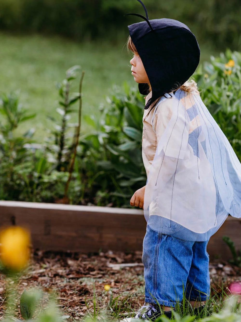 Child playing in a garden wearing bumble bee costume wings