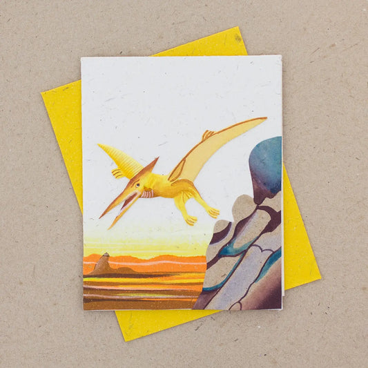 Handmade Greeting card with a yellow pterodactyl illustration on a desert landscape, placed on a matching yellow envelope 