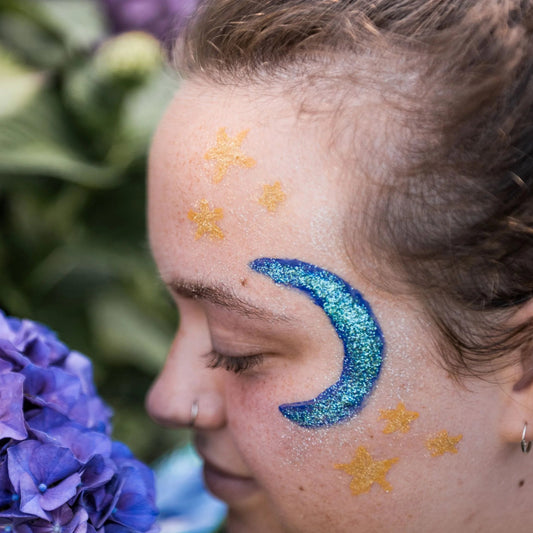 girl with natural earth face paint glitter featuring a blue crescent moon and yellow stars