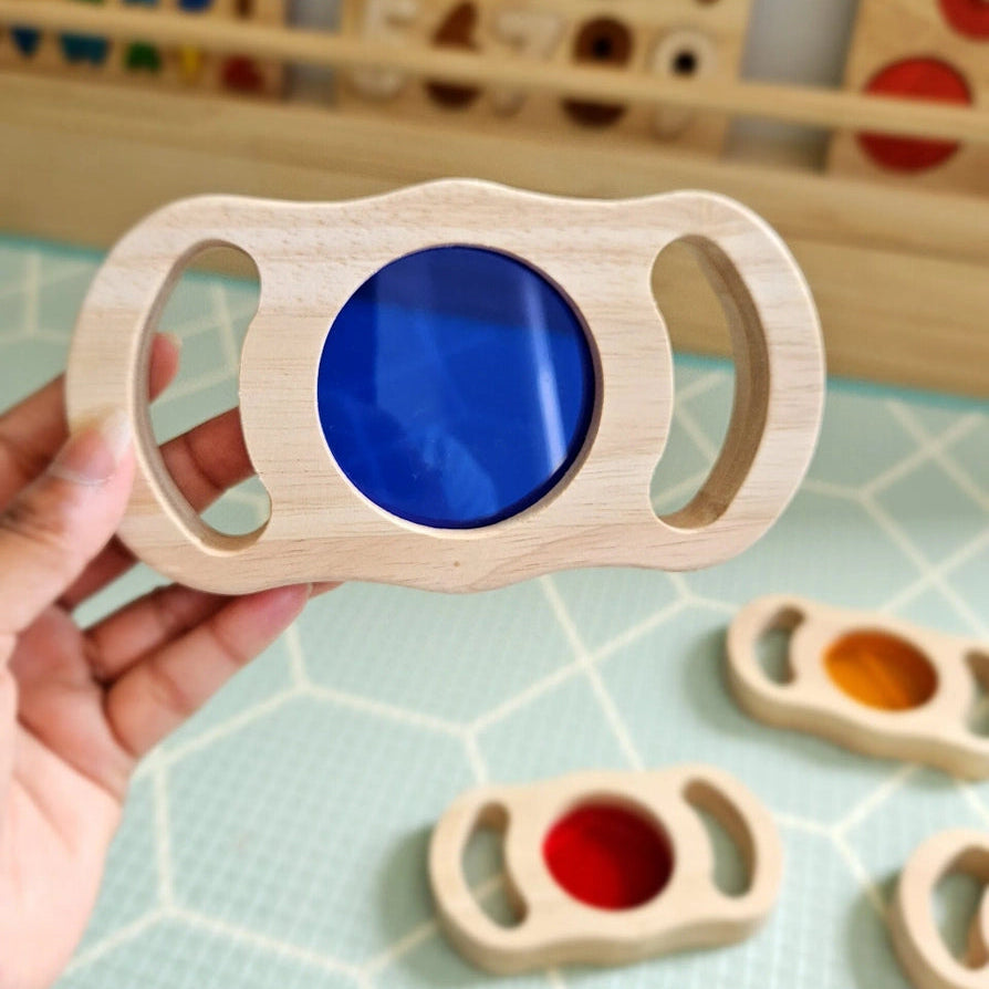 Person holding a wooden toy block with a blue lens 