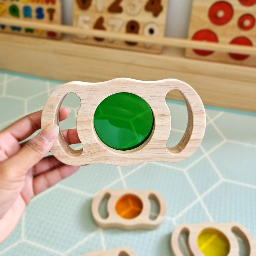 Wooden toy with a green lens held by a hand, with educational toys in the background.