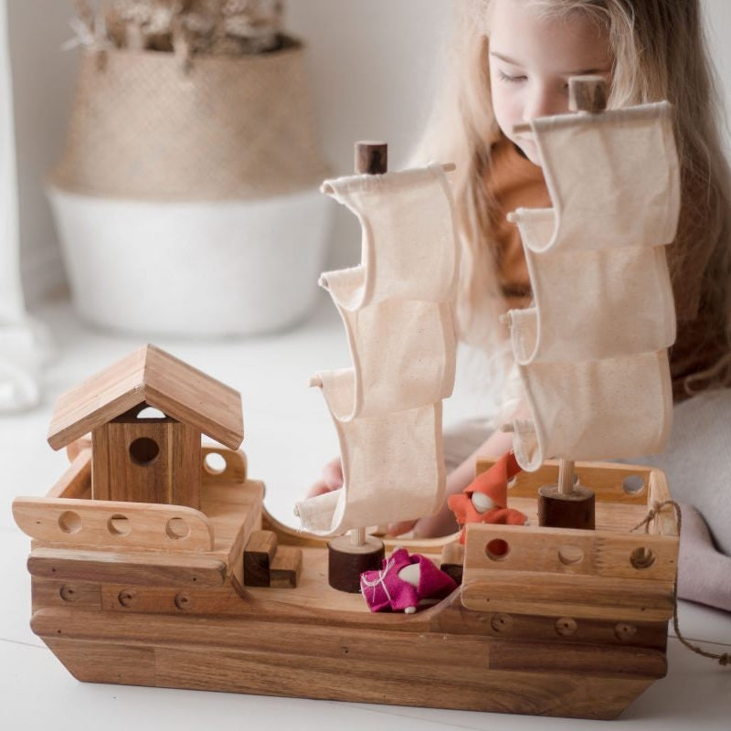 Girl playing with a wooden toy pirate ship and gnome dolls