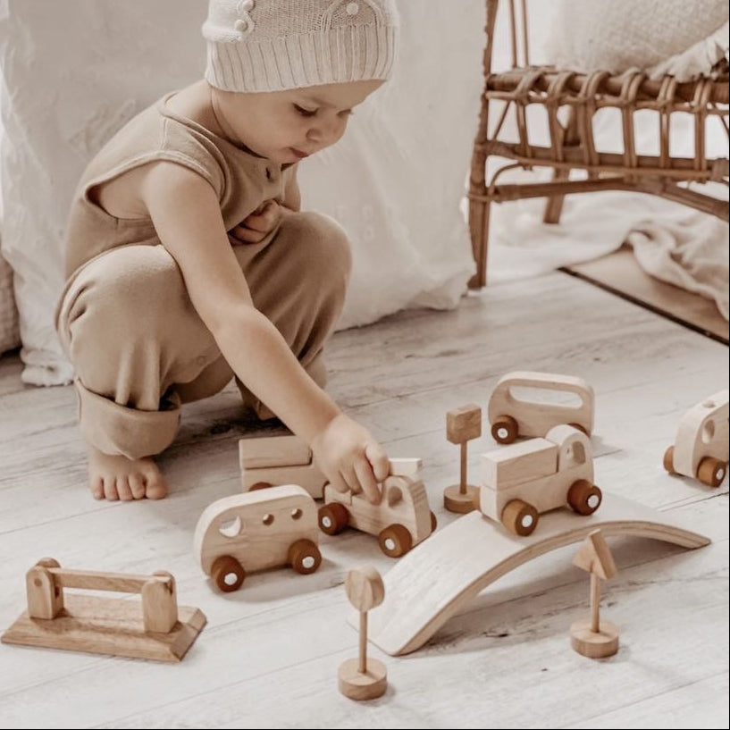 Child playing with wooden set of toy cars  and trucks with a bridge and road signs