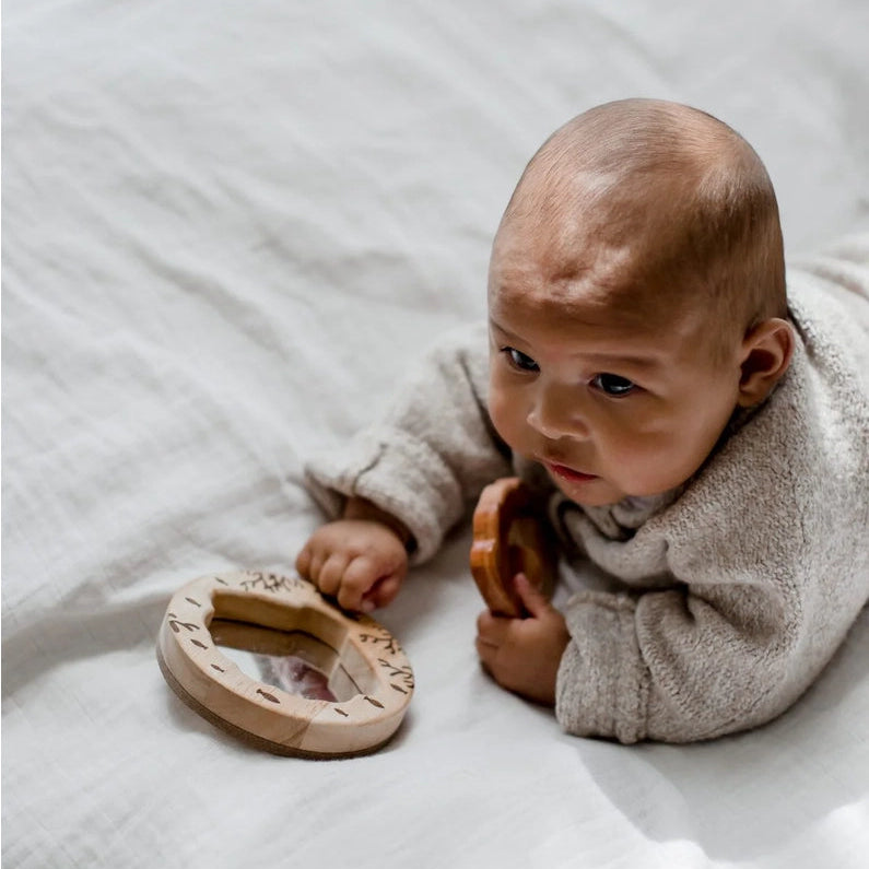Baby playing with a natural wooden mirror toy and shell rattle