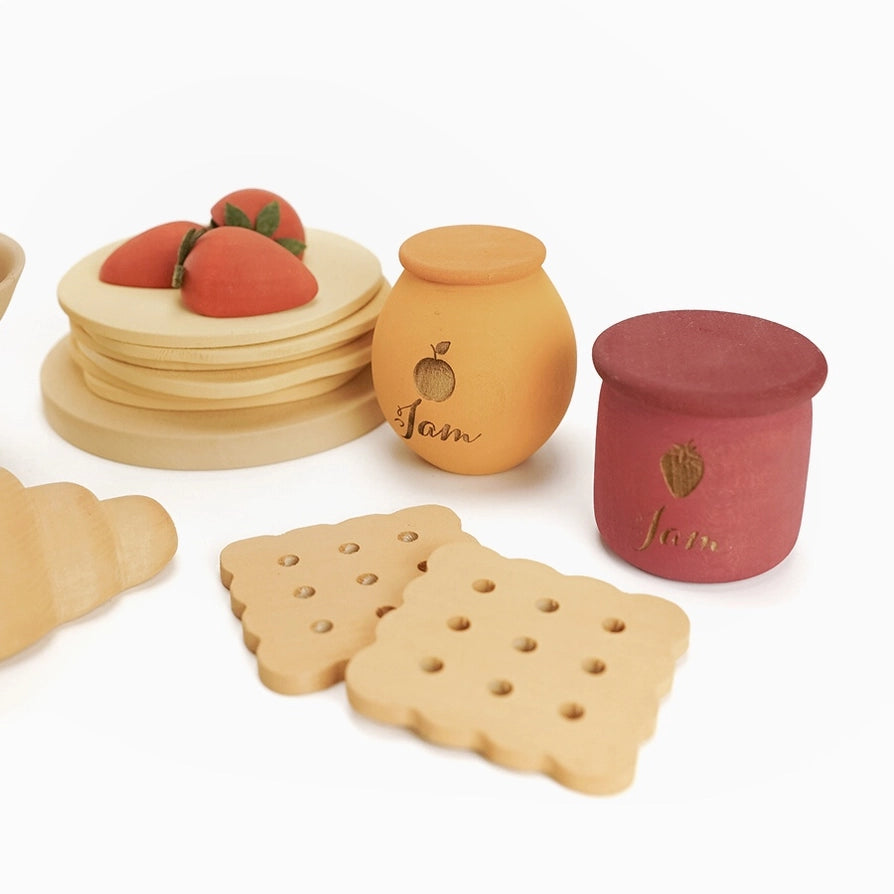 Sabo Concept set of wooden toy play food and containers, including a stack of pancakes on a plate with strawberries, jam jars, and two crackers.
