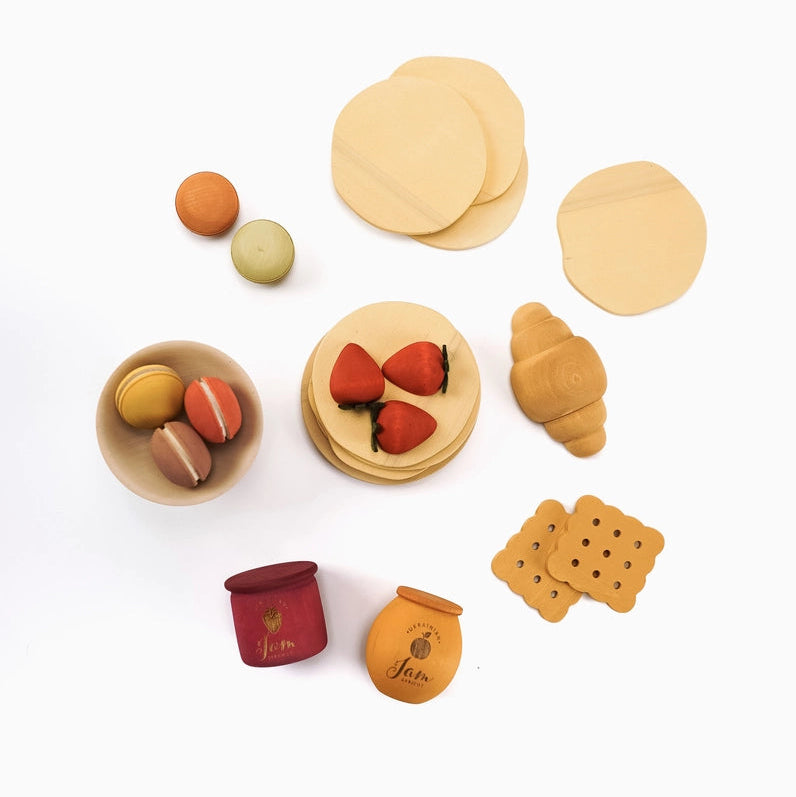 Sabo Concept children's wooden pretend play dessert set featuring light wood croissants, pancakes, strawberries, macarons, cookies, and small jars.