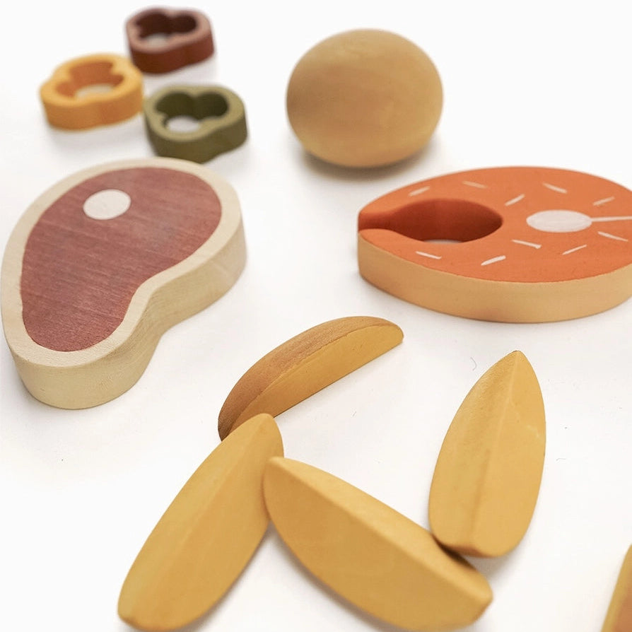 Sabo concept wooden play food dinner set for children, including a steak, roll, potato wedges, and sliced peppers.