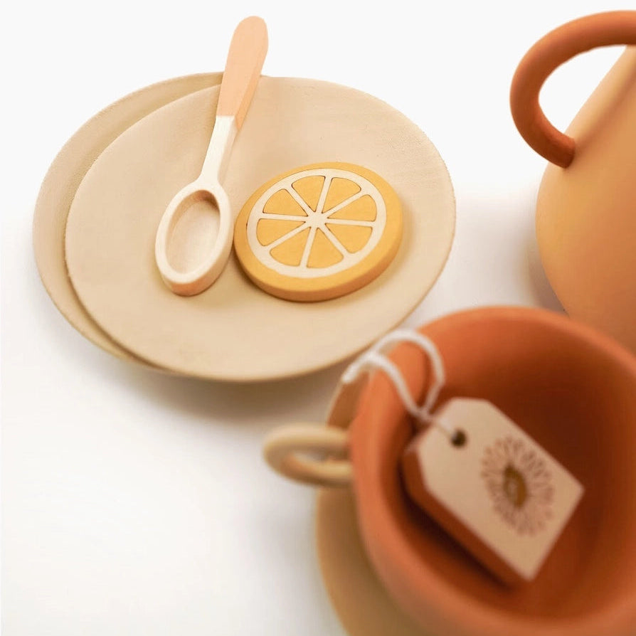  wooden toy tea-time accessories including a teapot, cup, spoon, saucer, and a lemon slice piece.