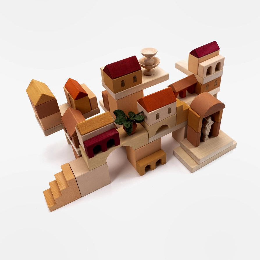 A set of wooden toy building blocks with houses in natural wood tones with painted red, orange, and brown roofs, arranged in an Italian Courtyard scene. 