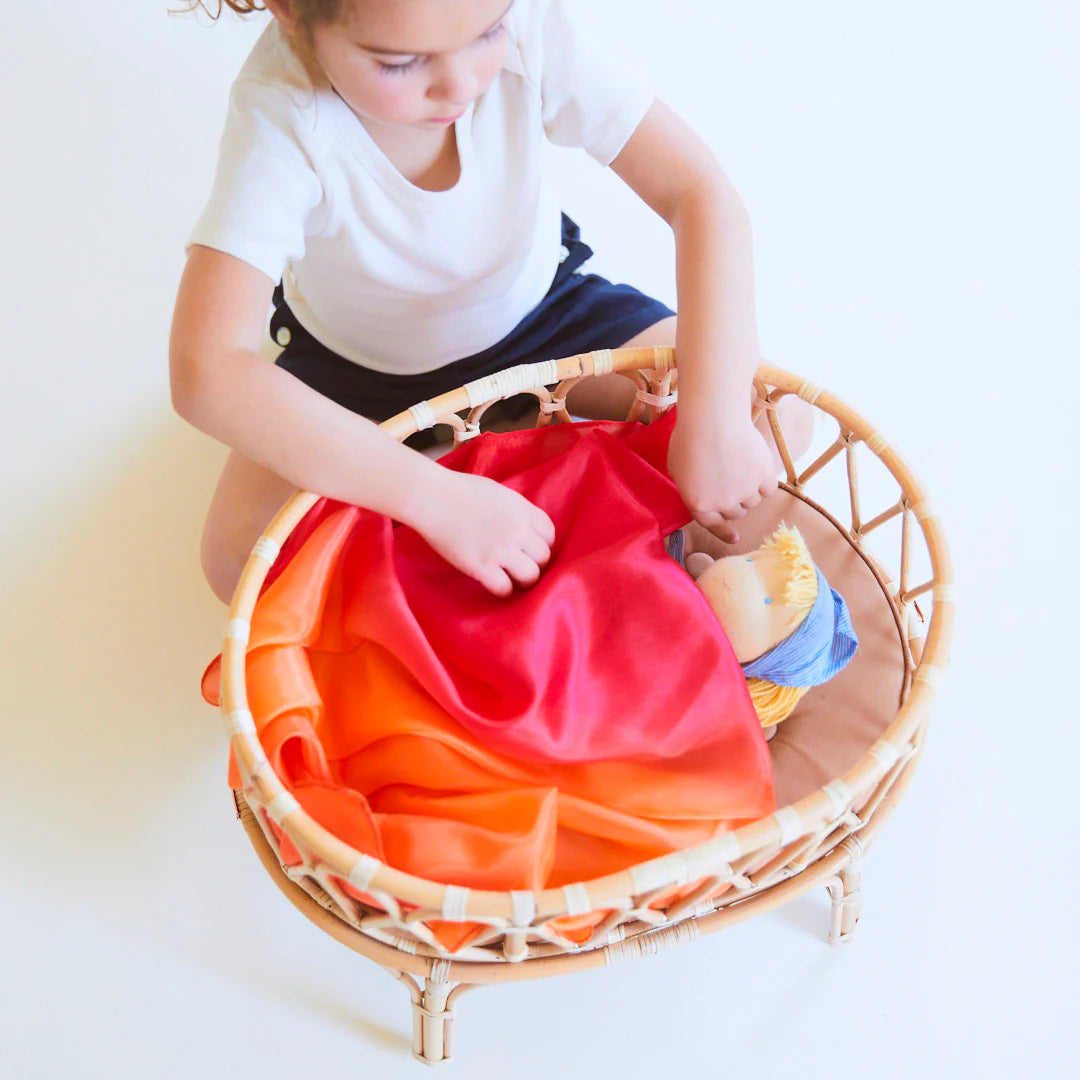 Child covering a doll with an enchanted fire playsilk. 