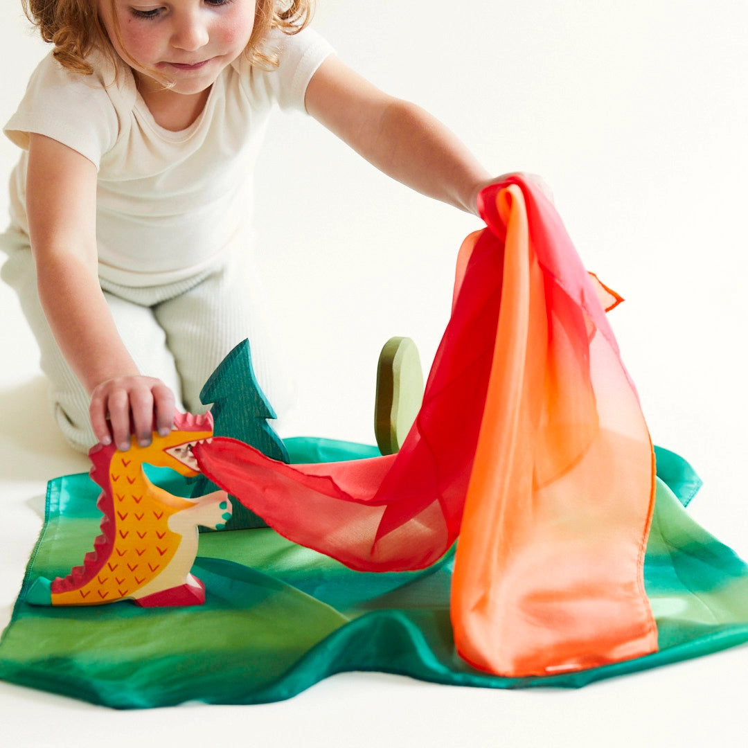 Child playing with forest and fire playsilks, a wooden dragon and trees