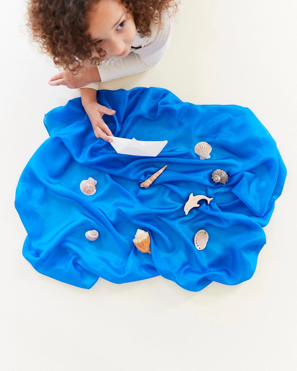 Child playing with a Sarah's silks solid royal blue playsilk as an ocean scene with sea life toys
