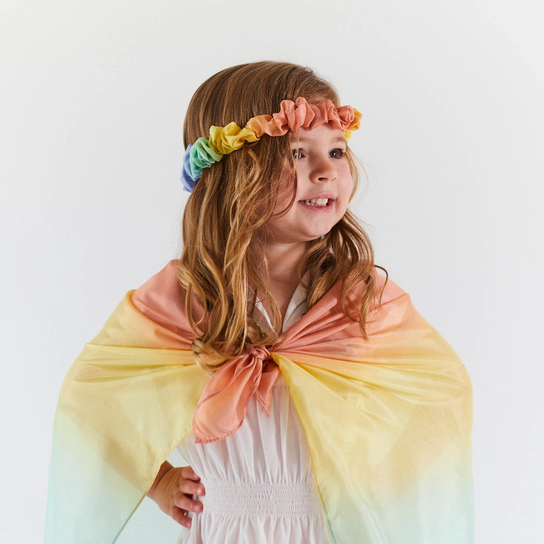 Young girl wearing a rainbow headband and colorful play silk cape 