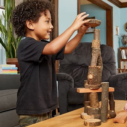 Boy playing with rustic giant wooden tree building blocks