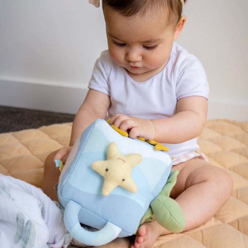 Baby playing with an organic soft plush ocean activity toy cube with a starfish, turtle, rattle, and a crab mirror