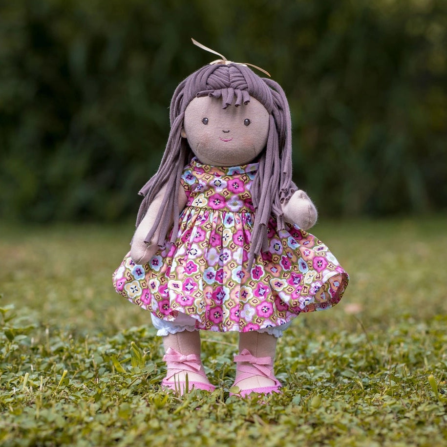 Soft jointed doll with long brown hair and floral dress standing on grass