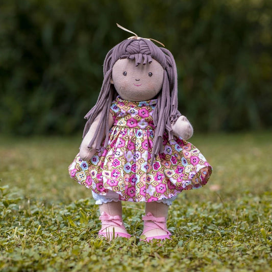 Soft jointed doll with long brown hair and floral dress standing on grass