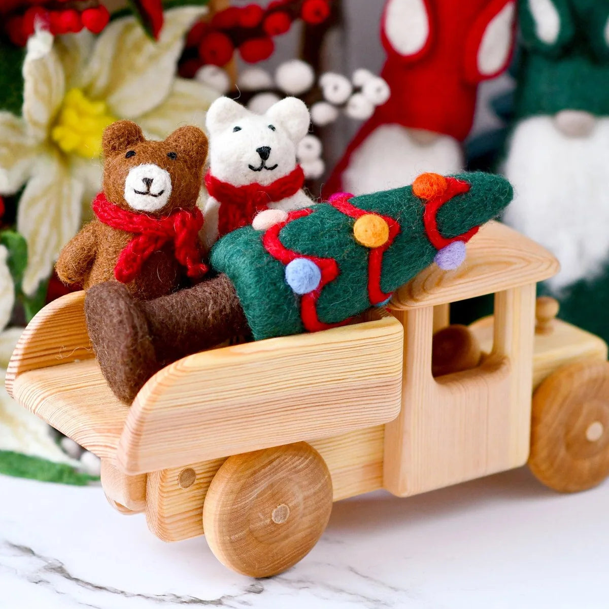 Tara Treasures felted Christmas tree toy in a wooden truck with felt bears standing nearby. 