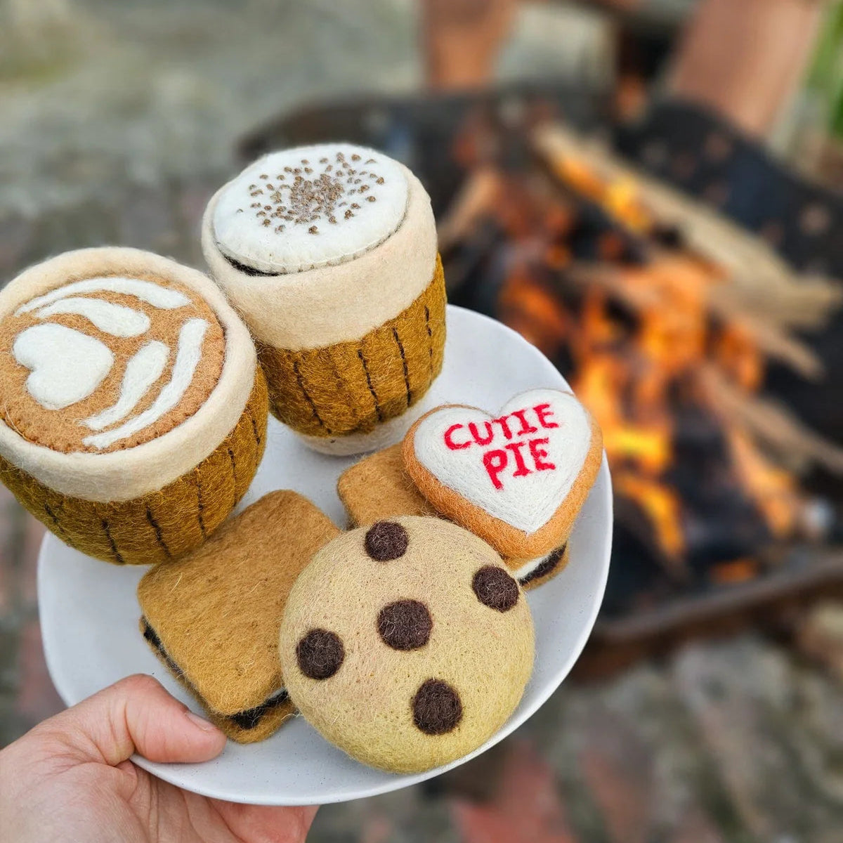 child holing felt play food cookies and coffee on a plate by a campfire