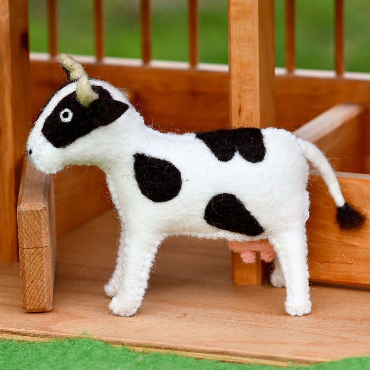 Tara Treasures felt cow farm animal small world toy next to a wooden barn