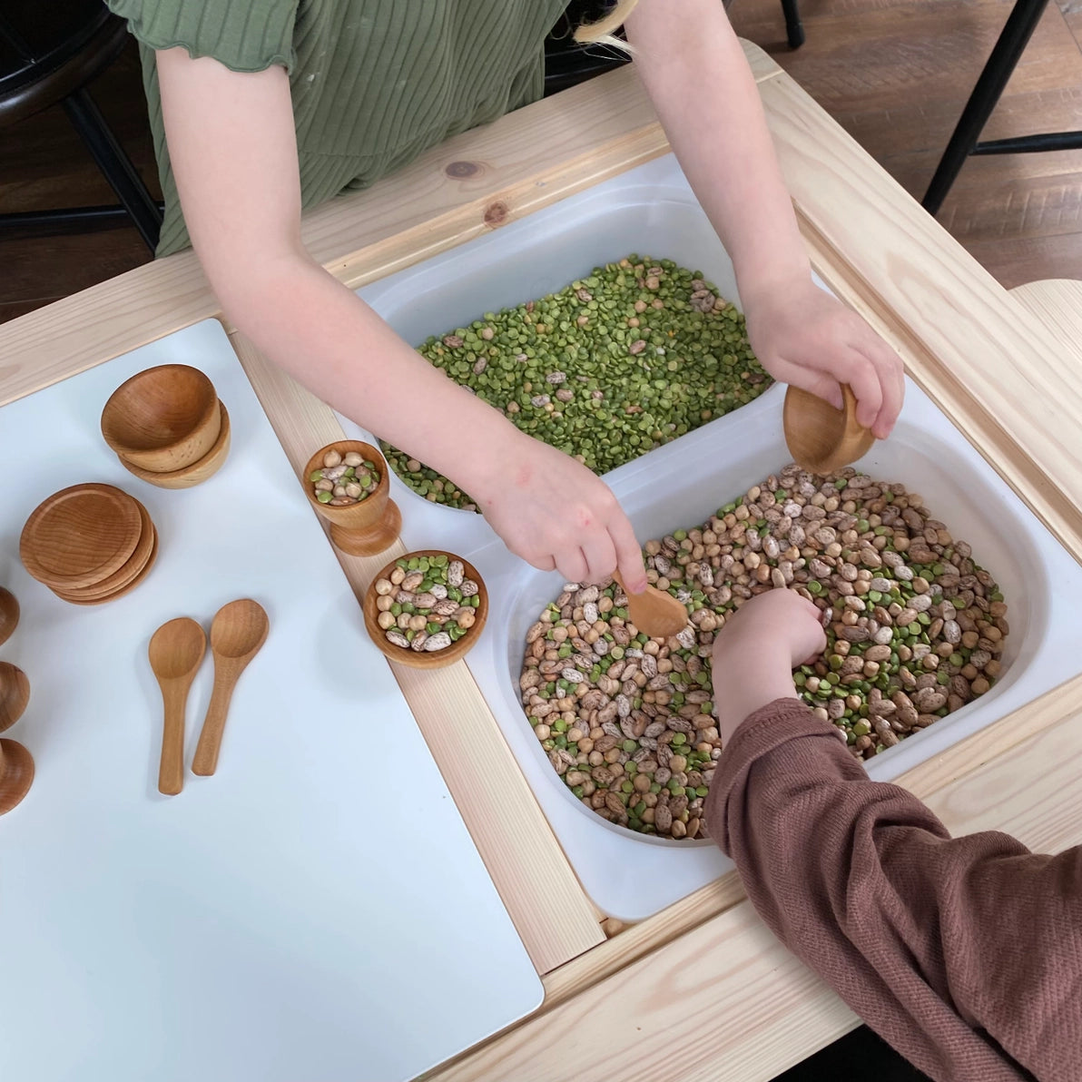 Children playing with wooden toy dish set in a Montessori sensory bin.