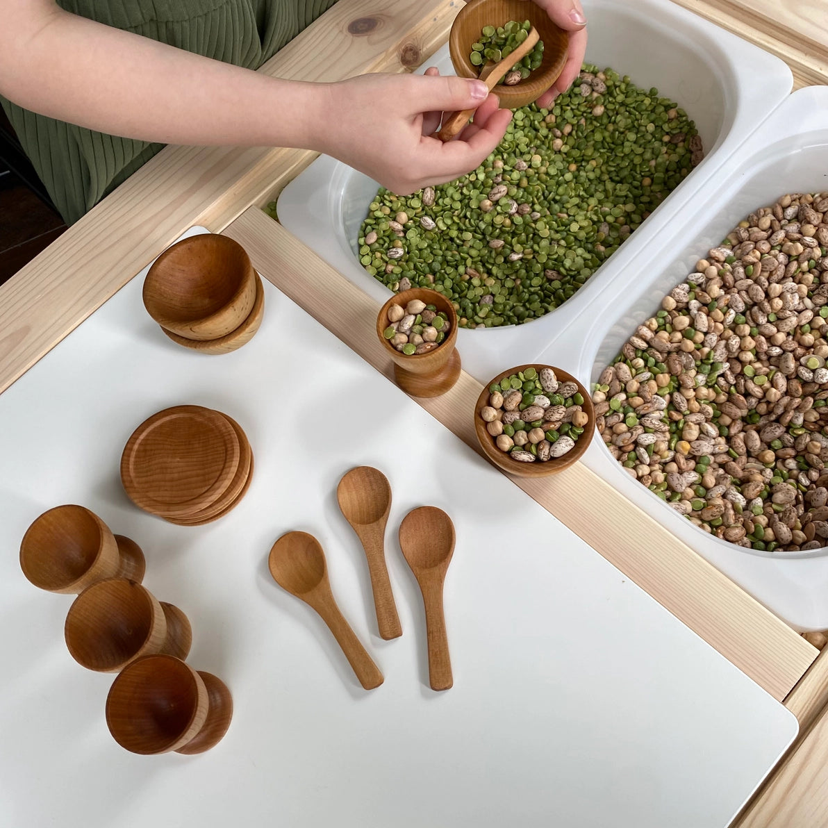 Girl playing with wooden  toy dish set in a Montessori sensory bin