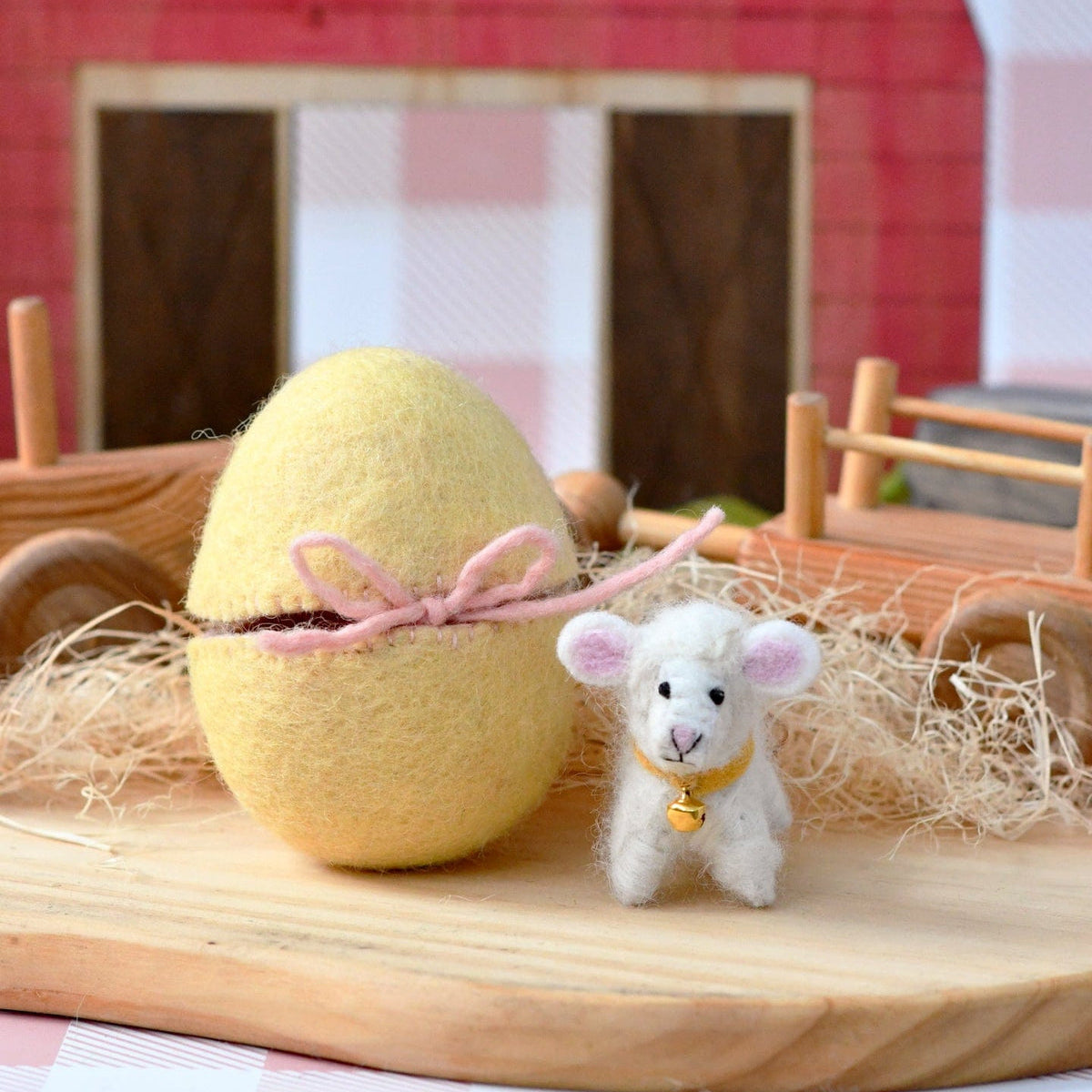 Tara Treasures yellow Easter egg with a pink bow and a small white lamb toy in front of a red barn