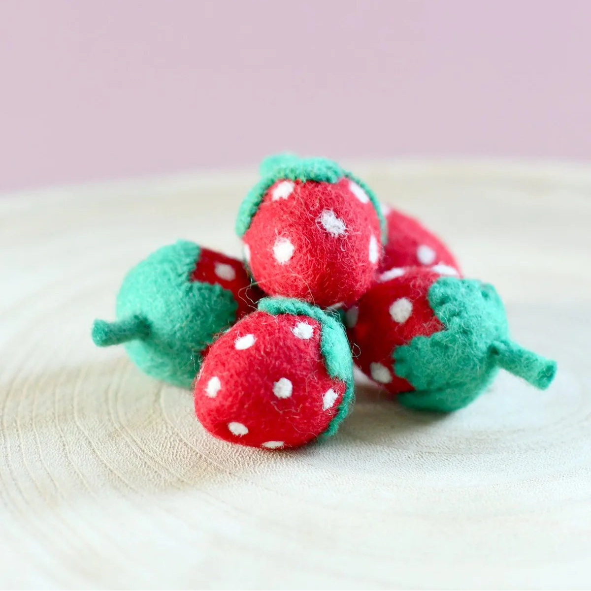 Felt strawberry toys with white polka dots on a light pink background