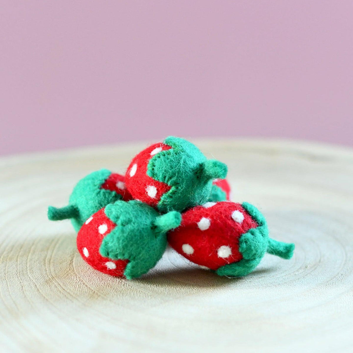 Red and green felt strawberry toys on a wooden surface 
